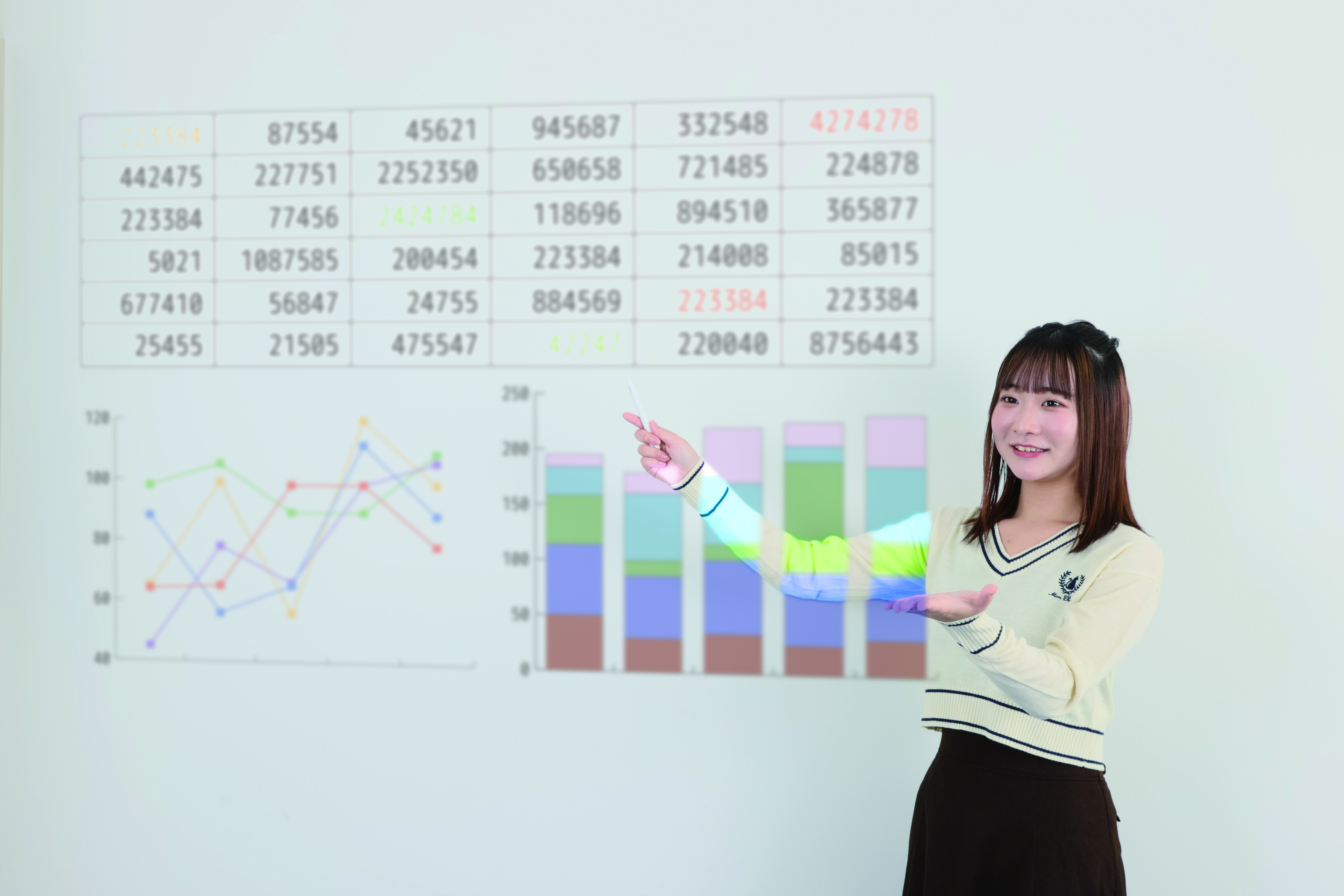 プレゼン資料のグラフと表を指さしながら説明する女子学生。