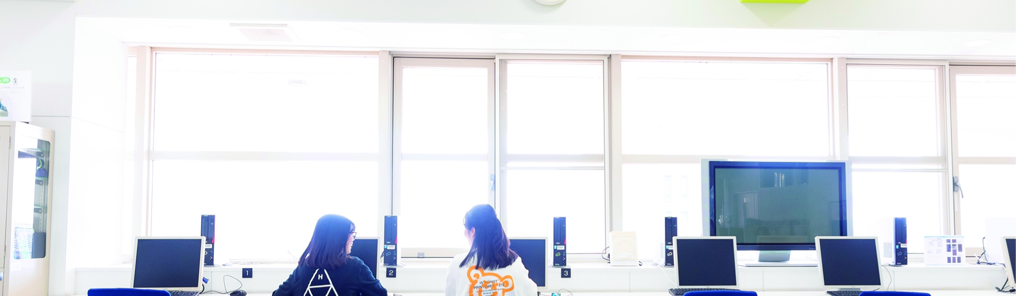 コンピュータ室で並んで作業をする女子学生たちの後ろ姿。