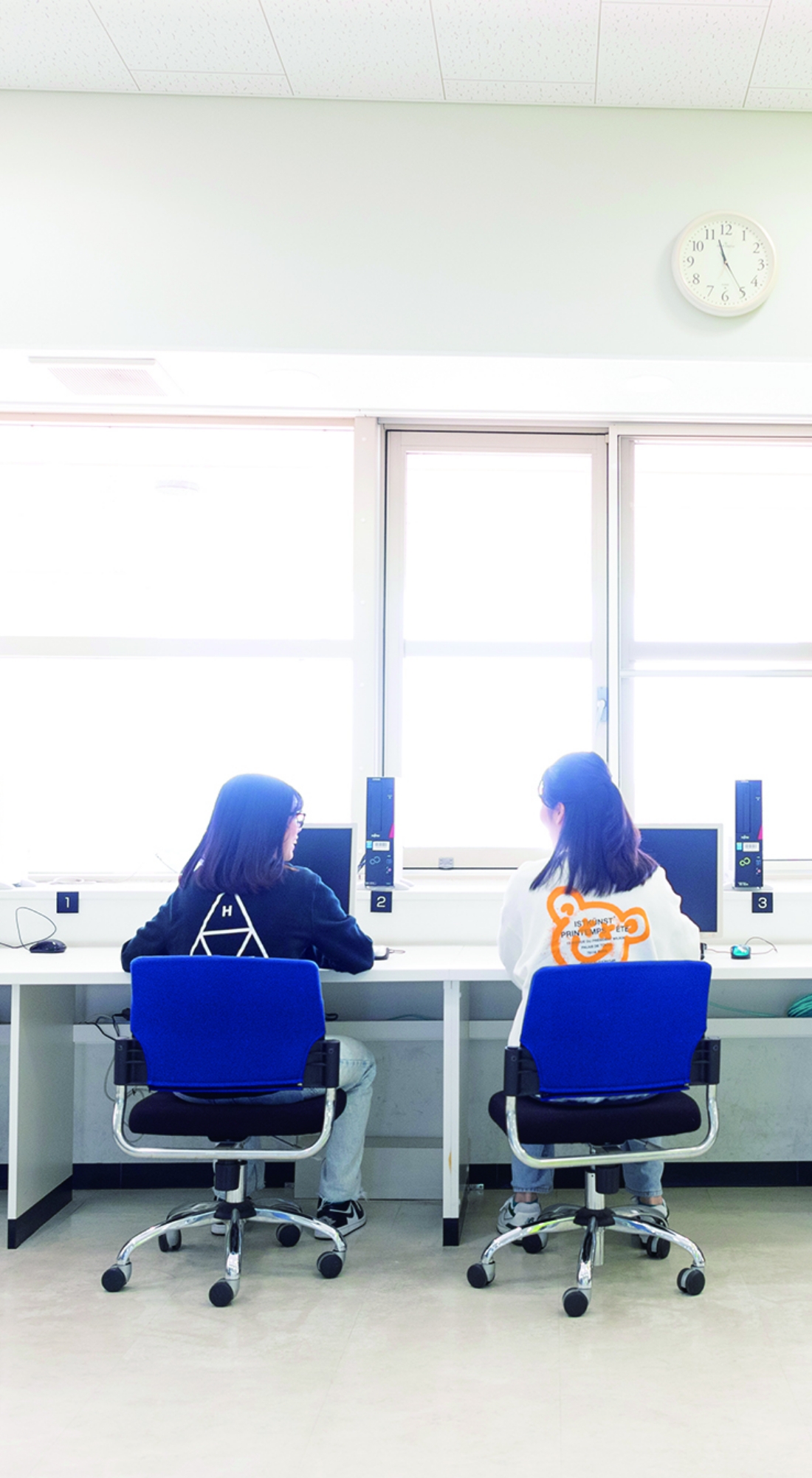 コンピュータ室で並んで作業をする女子学生たちの後ろ姿。