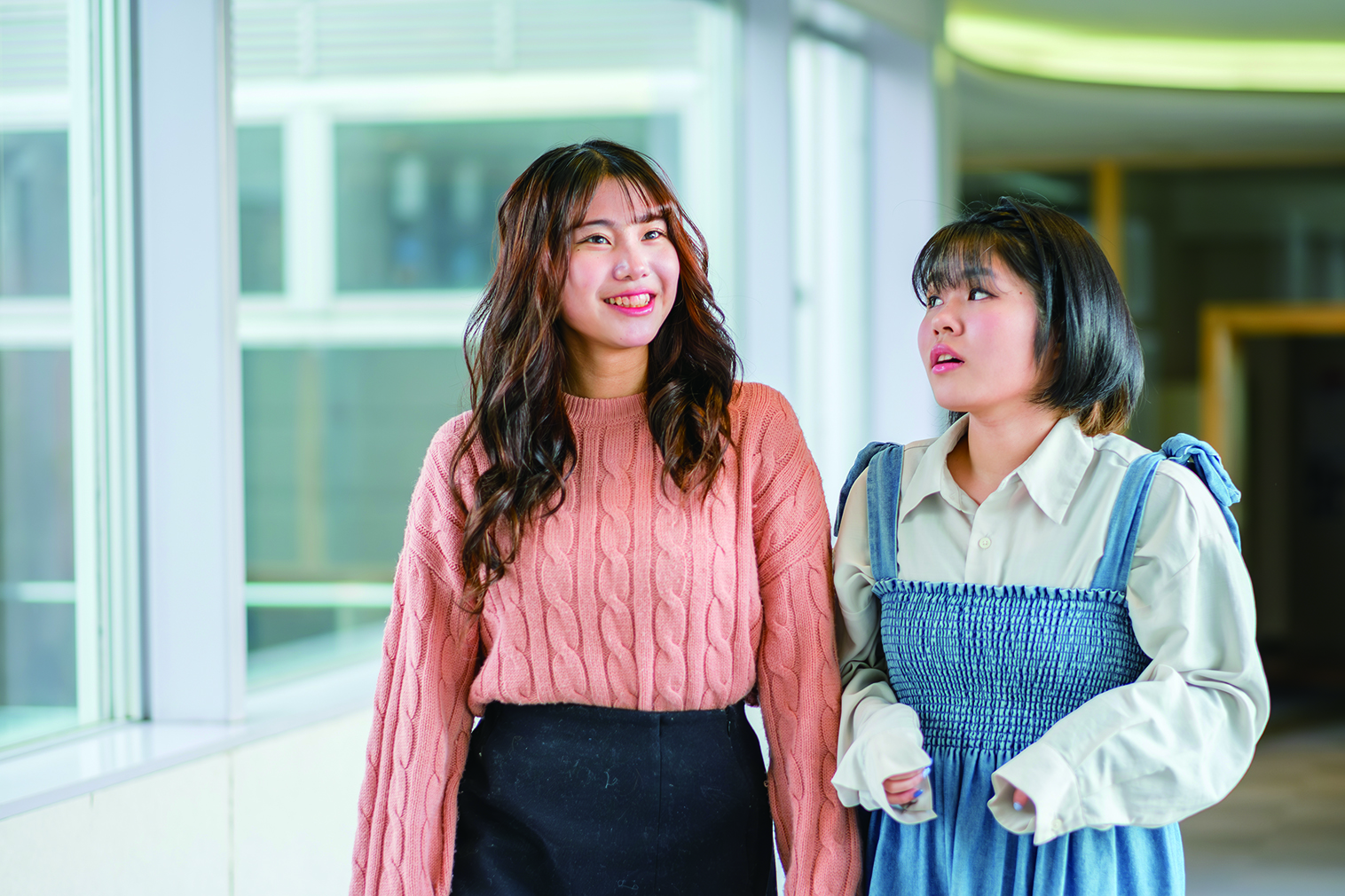 校舎の廊下を歩きながら談笑する2人の女子学生。
